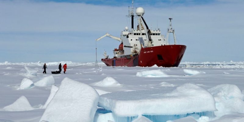 Three people pulling a sledge towards a ship in Arctic ice