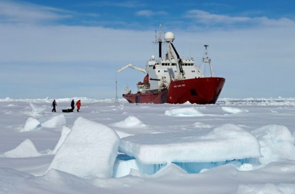 Three people pulling a sledge towards a ship in Arctic ice