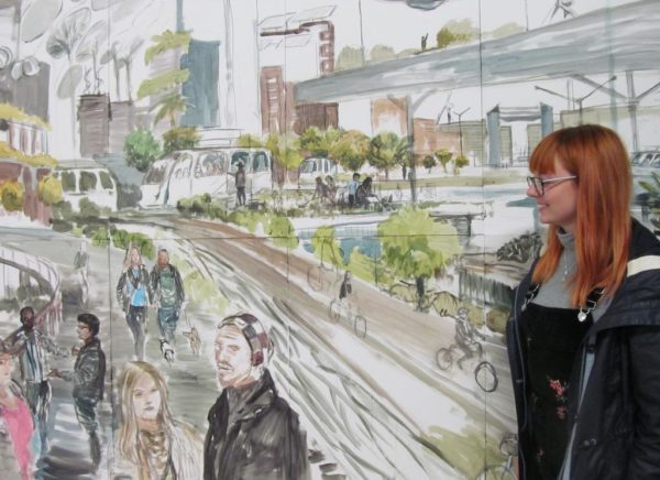 A young lady standing in front of a watercolour painting of a futuristic view of a city