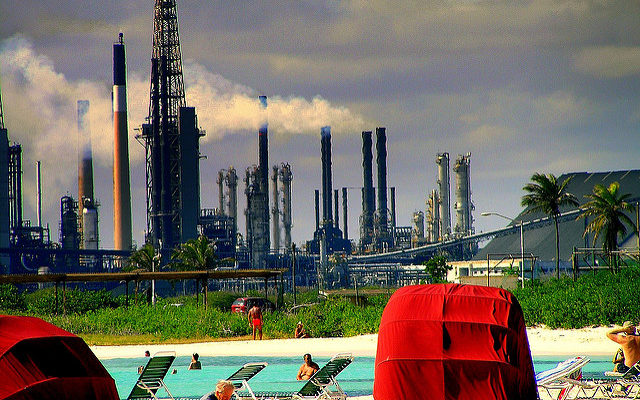 People relaxing at a poolside, with an oil refinery working in the back