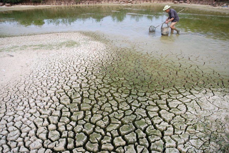 Man with fishing net and bucket in a depleted river with the banks revealing cracked earth