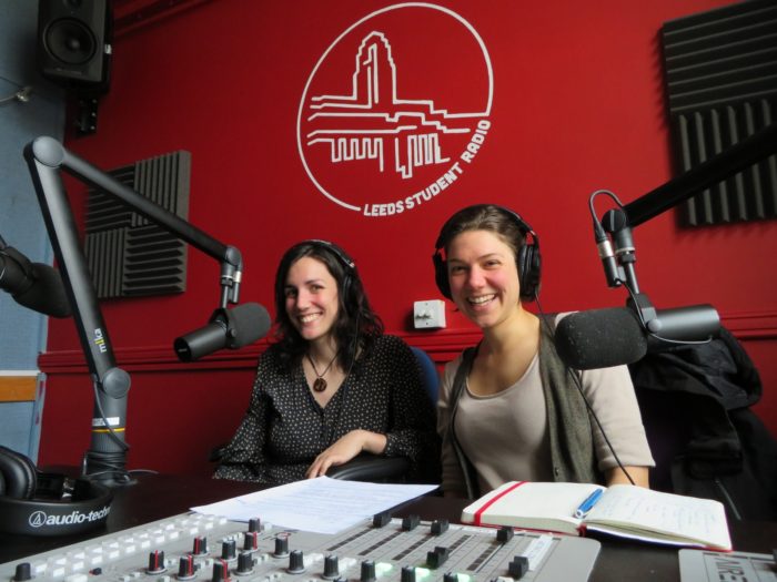 Two young ladies in Leeds Student Radio recording studio, smiling into the camera
