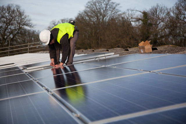 Man in protective clothing installing solar panels on a building roof