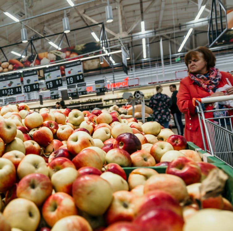 Woman with shopping trolley looking at display of apples