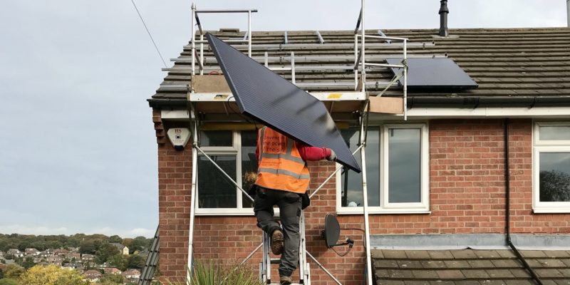 Man takes solar panel up a ladder to fit on the roof of a house