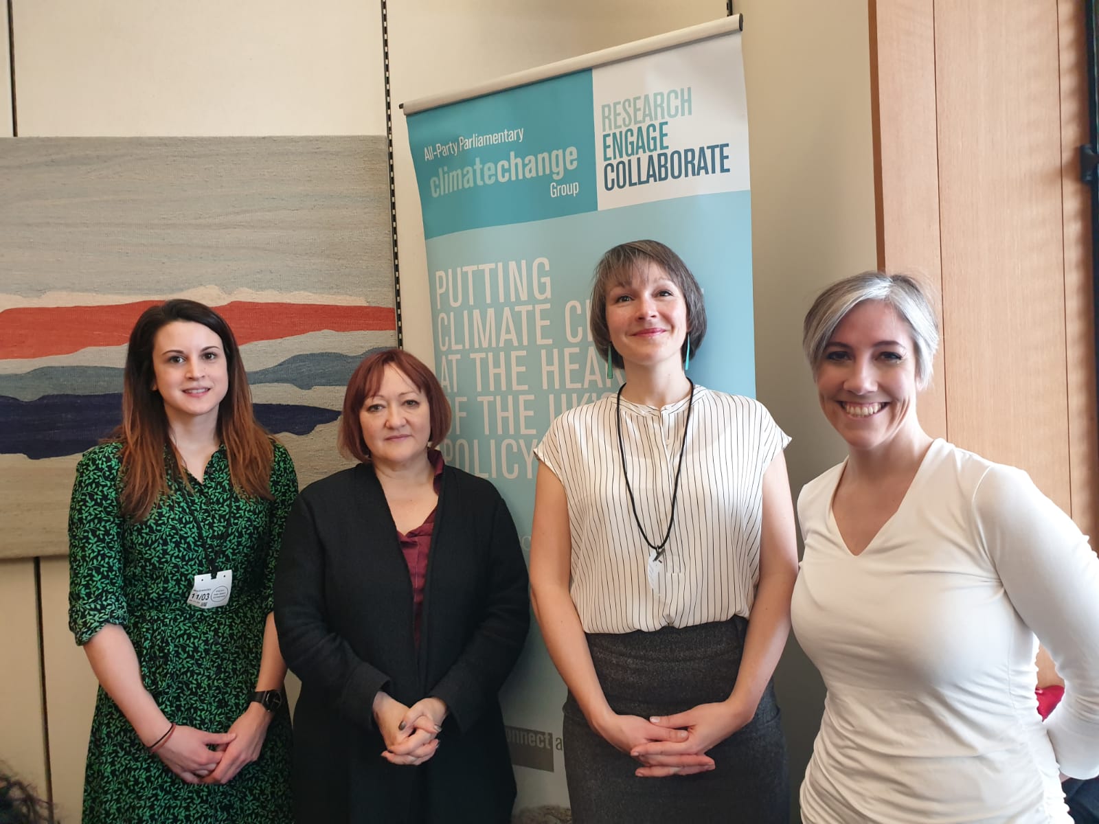 Four female researchers standing in front of a pop-up banner advertising the All-Party Parliamentary Climate Change Group