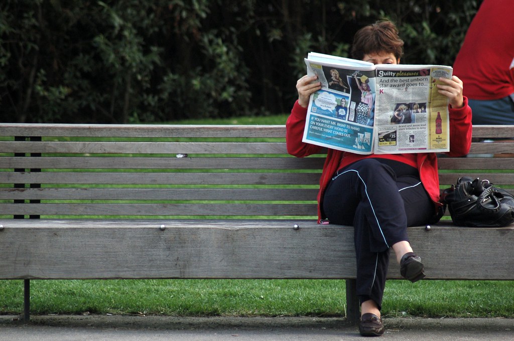 Lady reading newspaper on a bench