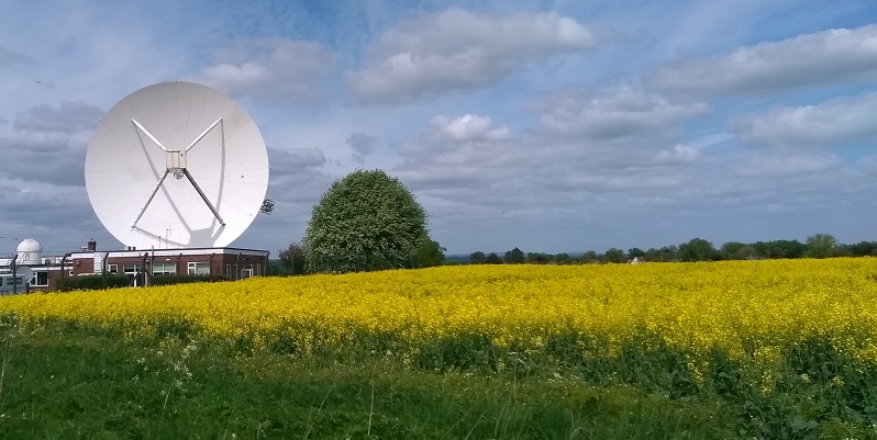 A large weather radar dish in a green field on a sunny day