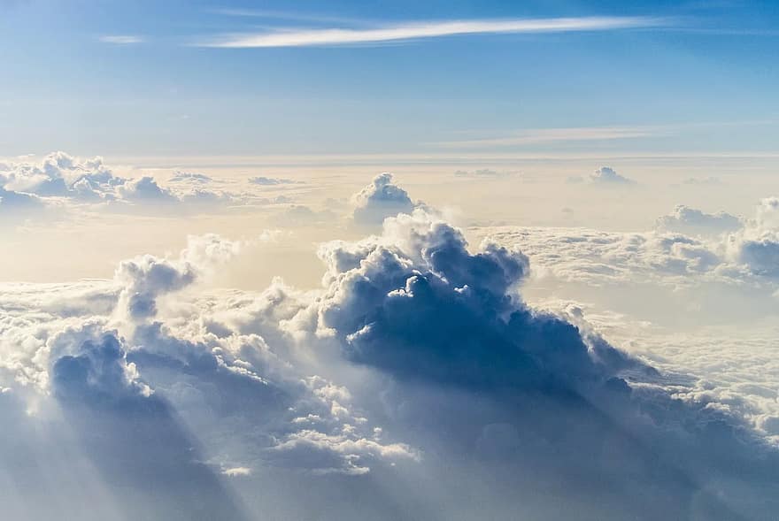 Clouds seen from above the cloud line, with blue sky behind and sunlight cutting through