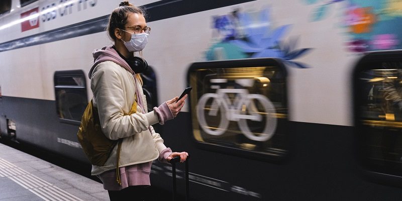 Woman in mask stands next to train