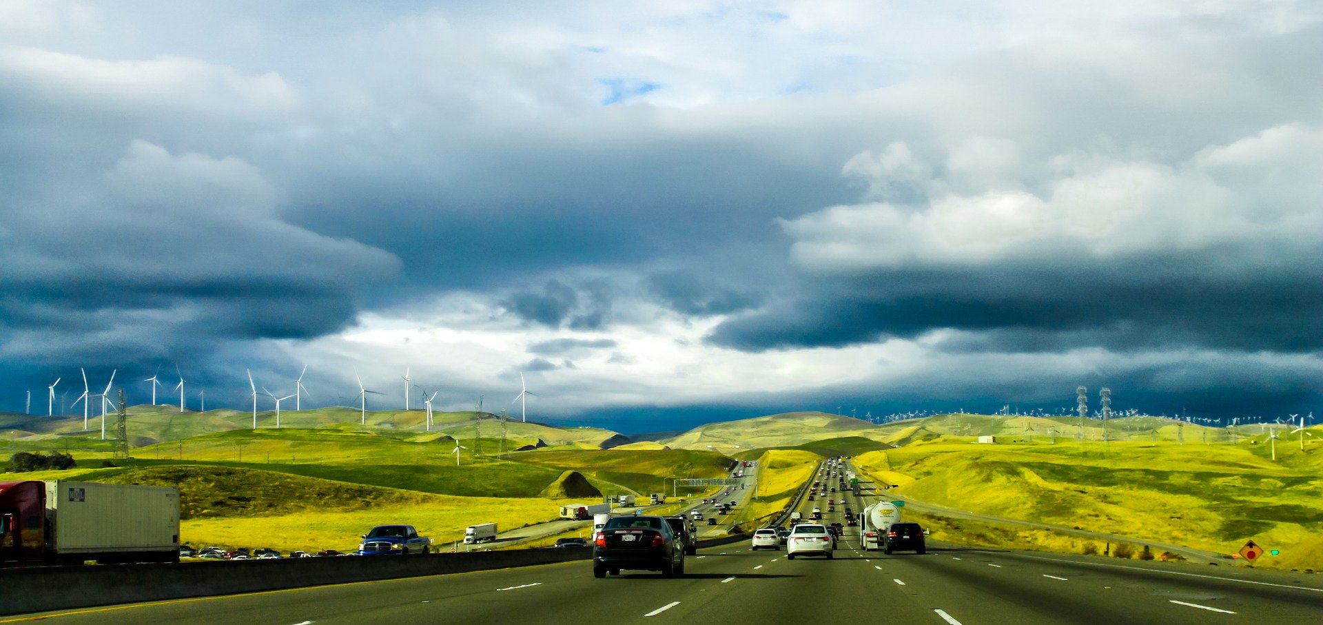 Cars drive down a highway with windmills in shot and a moody blue-grey sky