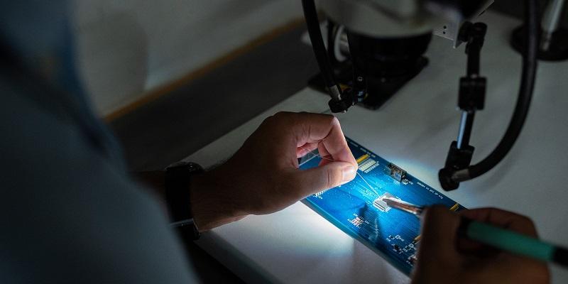 Hands manipulating a circuit board under a microscope