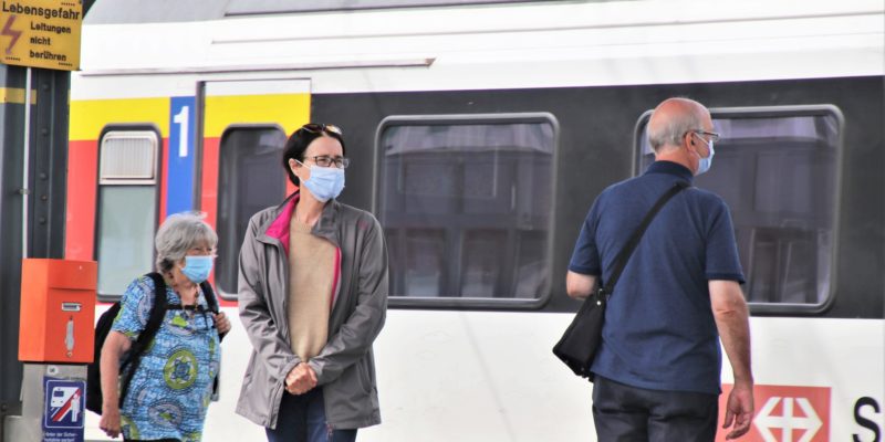 Three people wear masks waiting to board a train
