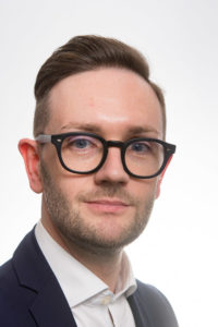 A portrait of Chris Stark. Chris is a white male with short brown hair and beard. Chris is wearing round black glasses.