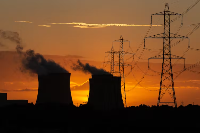 Power station and transmission towers in front of a bright orange sunset.