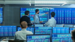Three people discussing information displayed on several screens behind them