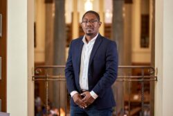 Professor wearing a blazer and shirt smiling at the camera inside of a library